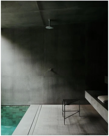 Modern bathroom interior featuring a minimalist design with dark grey walls, a walk-in shower, and a sleek metal stool, showcasing contemporary style.