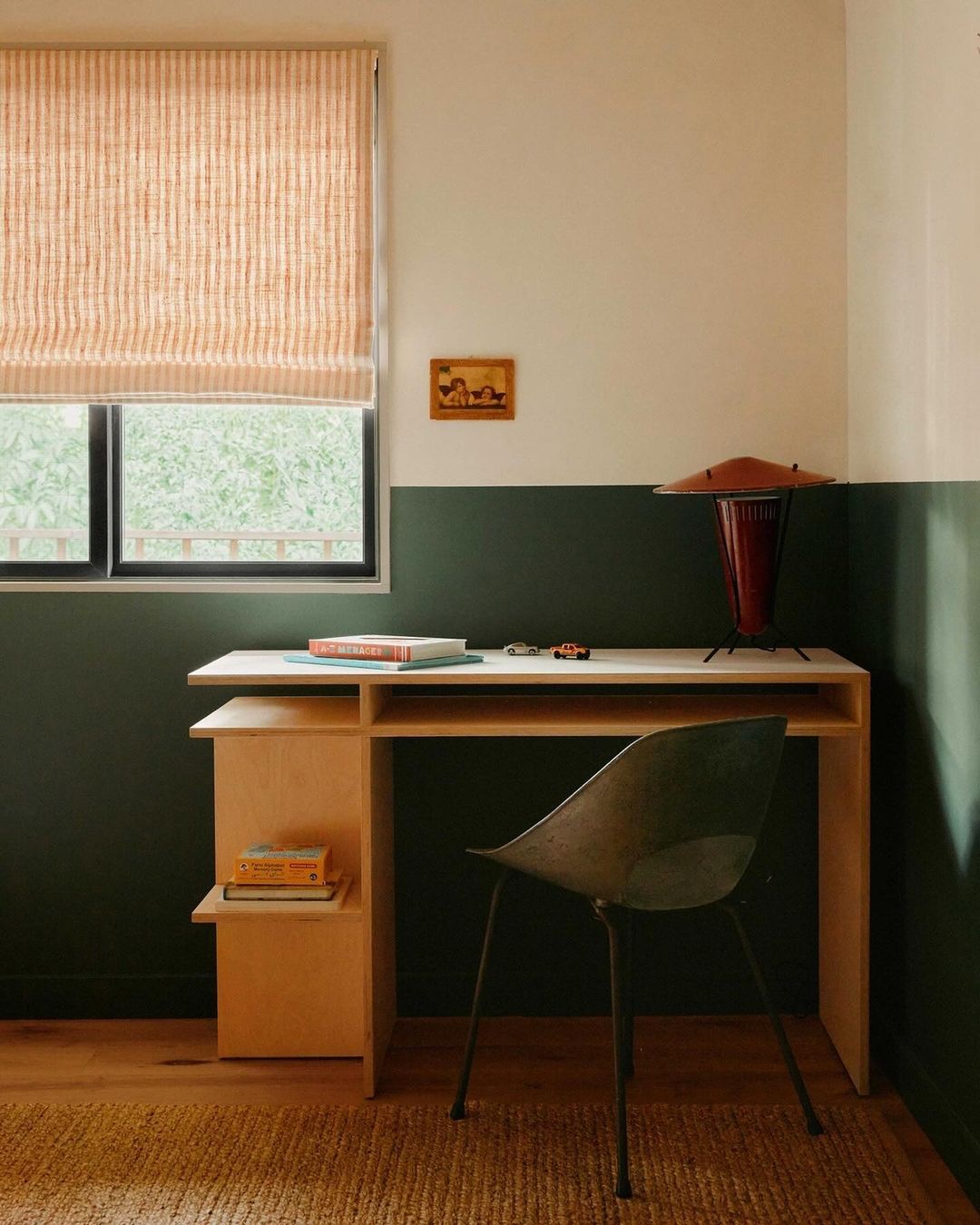 Modern home office setup with a light wood desk, green chair, and window with blinds, creating a minimalist workspace aesthetic.