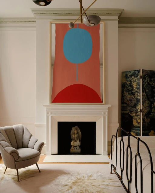 Bedroom interior with an abstract painting above the fireplace, featuring a gray chair, folding screen, and wrought iron bed frame.