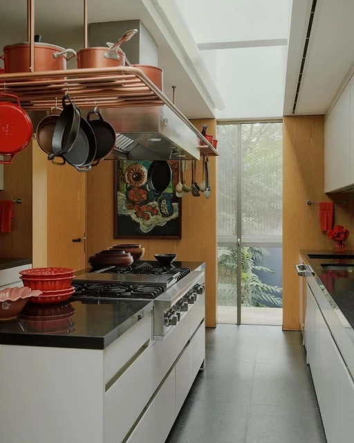 Modern kitchen interior featuring a large island, stainless steel appliances, and copper pot rack with hanging cookware.