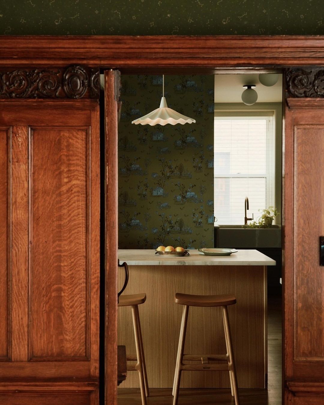 Interior view of a kitchen with custom wood cabinets, an island with stools, and an overhead pendant light.