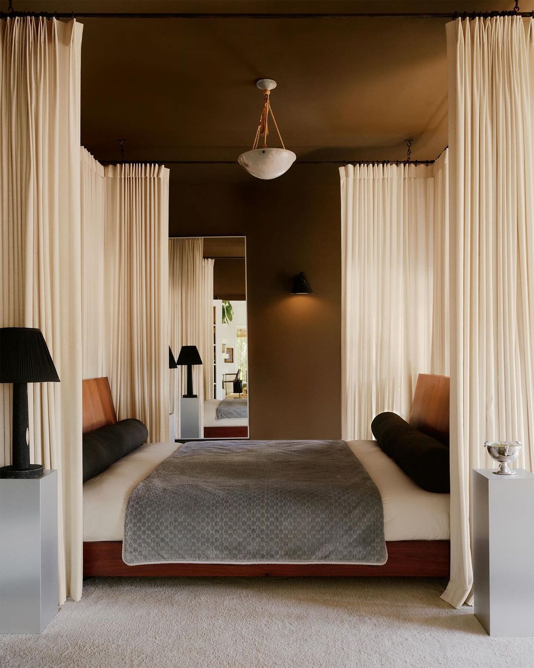 Bedroom interior with a king-size bed featuring white drapery, alongside black lamps on aluminum stands, creating a luxurious and tranquil space.