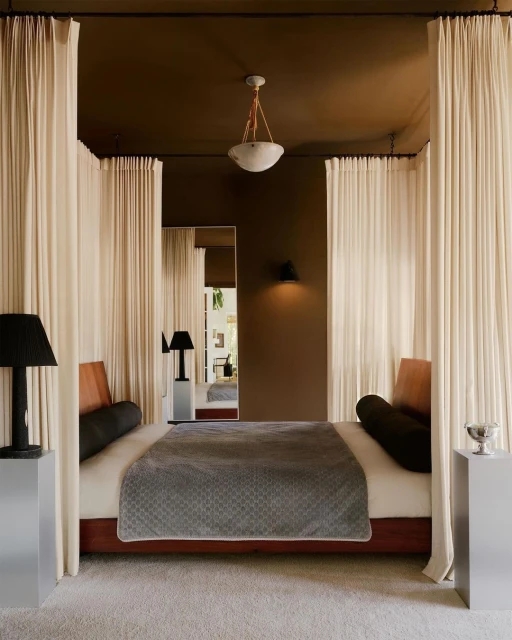 Bedroom interior with a king-size bed featuring white drapery, alongside black lamps on aluminum stands, creating a luxurious and tranquil space.