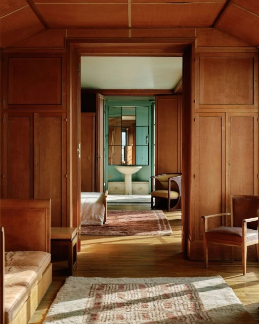 Classic interior view through a doorway showing a bedroom and a bathroom. Wood paneled walls and patterned rugs add to the traditional style.