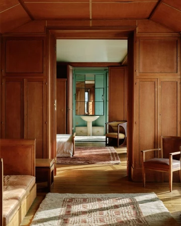 Classic interior view through a doorway showing a bedroom and a bathroom. Wood paneled walls and patterned rugs add to the traditional style.