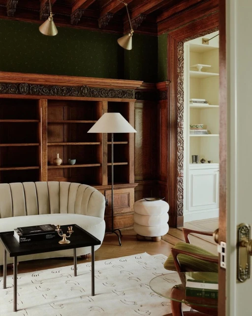 Living room interior showcases a cream-colored sofa, dark coffee table with books and candles, a lamp, and a decorative patterned rug.