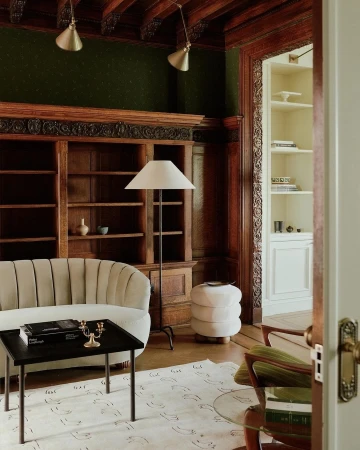 Living room interior showcases a cream-colored sofa, dark coffee table with books and candles, a lamp, and a decorative patterned rug.