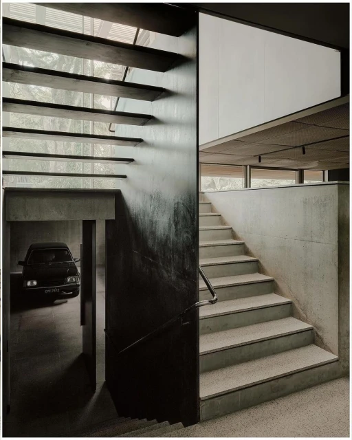 Architectural design featuring concrete stairs, a garage with a vintage car, and natural light filtering through wooden slats above.