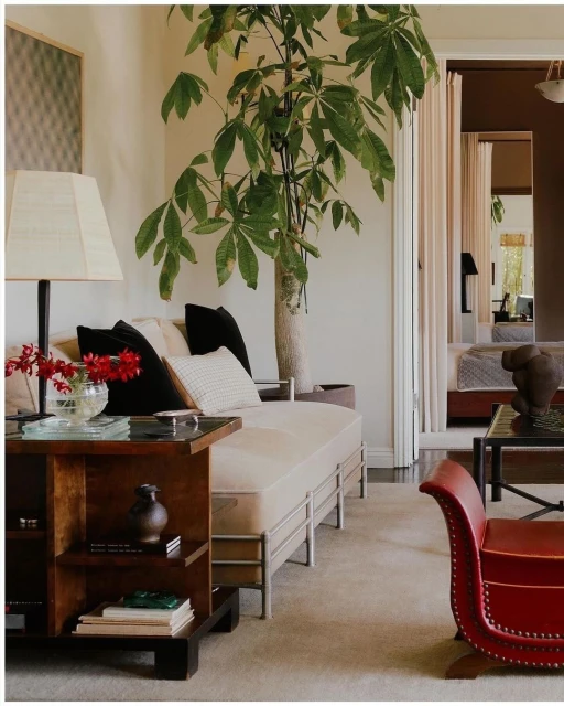 Interior of a living room featuring a sofa, wooden side table with flowers, and a large potted plant, creating a cozy and inviting space.
