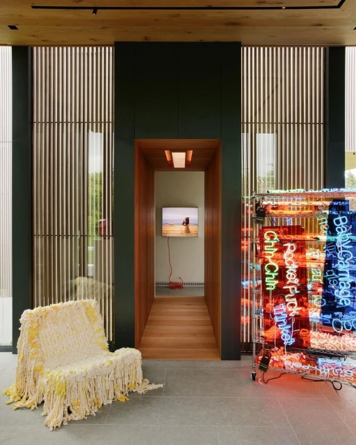 Interior view of modern home with bright neon art, a shaggy chair, and a view into another room with a wall-mounted television.