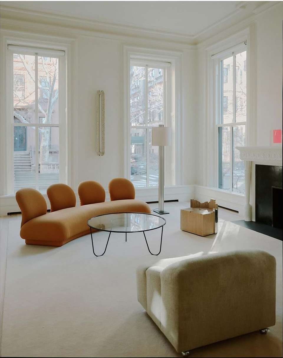 Living room interior featuring modern furniture: a curvilinear sofa, a round glass coffee table, and an armchair. Natural light floods the space.