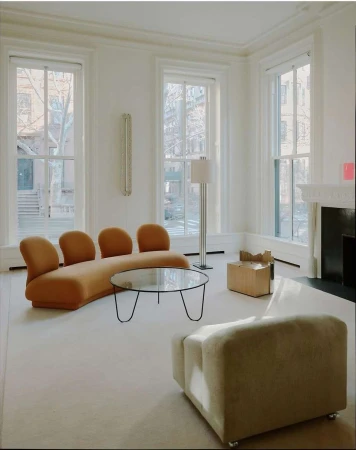 Living room interior featuring modern furniture: a curvilinear sofa, a round glass coffee table, and an armchair. Natural light floods the space.