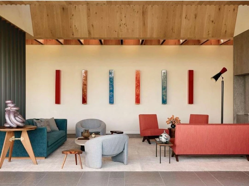 Living room interior featuring mid-century modern furniture, colorful wall art, and natural light through large windows and wood ceiling.