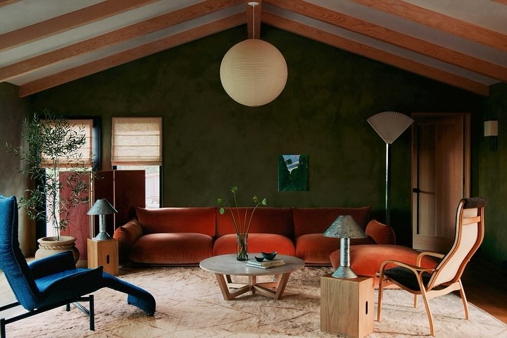 Living room interior with an orange sofa, a blue chair, and a beige rug, complemented by wooden beams and a large spherical lamp.