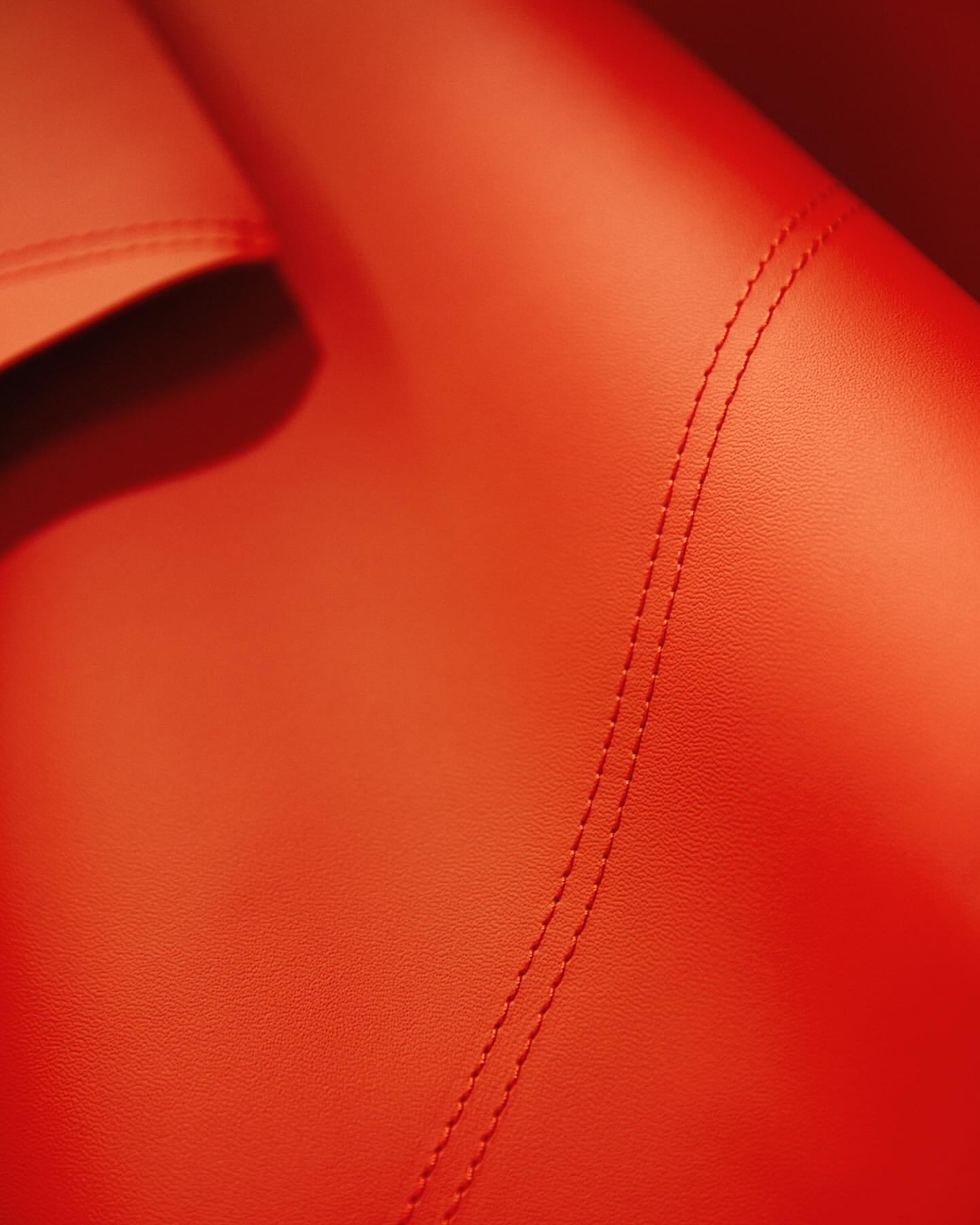 Close-up of textured leather in shades of orange, showcasing detailed stitching. Automotive and interior design material.