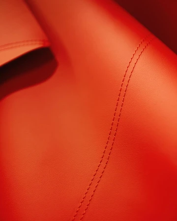 Close-up of textured leather in shades of orange, showcasing detailed stitching. Automotive and interior design material.
