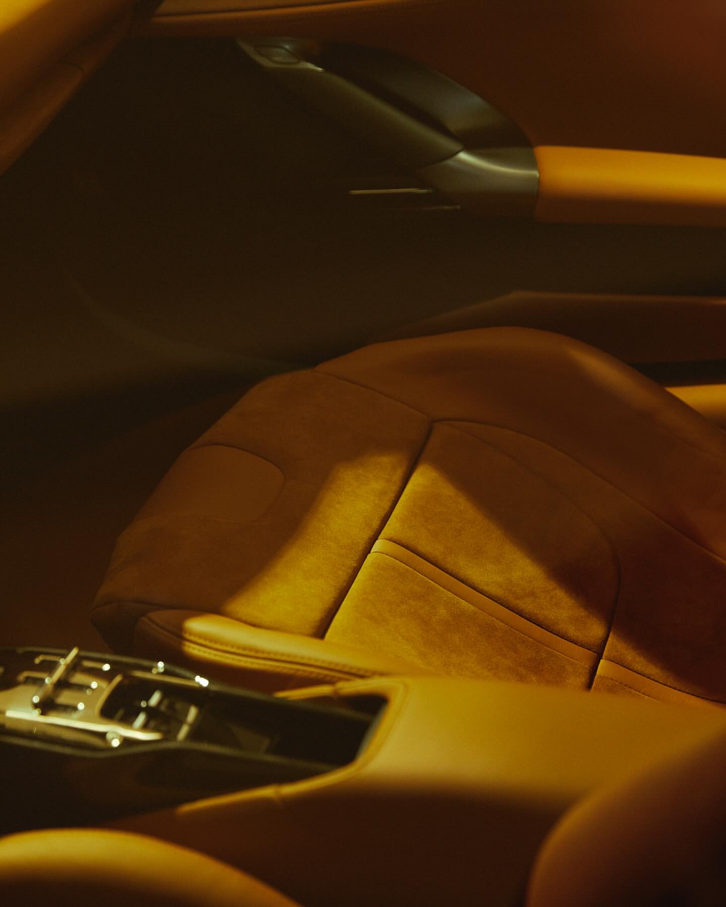 Close-up of car interior showing a leather car seat with a center console.  Warm, brown tones are used throughout the interior.