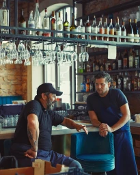 Two men in a bar interior with liquor shelves and hanging glassware by photographer William Lacalmontie in Paris