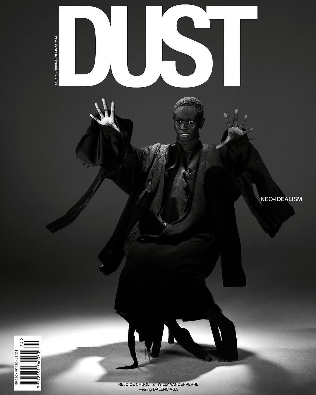 Black-and-white magazine cover featuring a dark-skinned model in an abstract pose, adorned in dark clothing, against a gray backdrop.