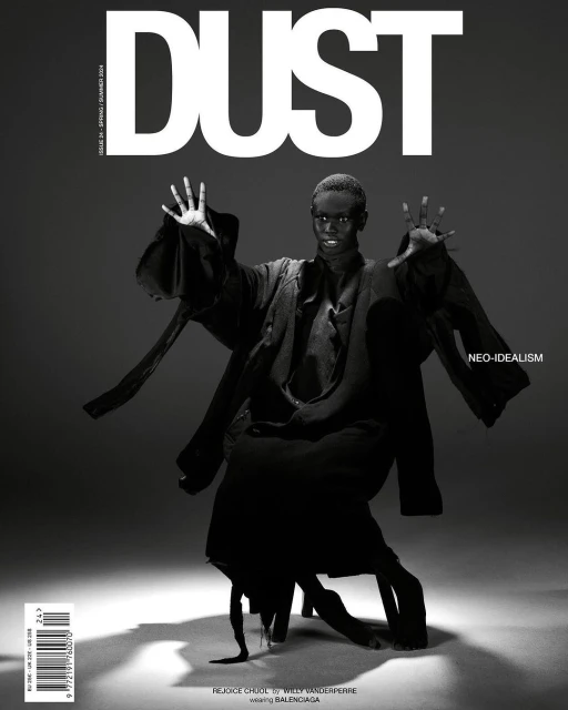 Black-and-white magazine cover featuring a dark-skinned model in an abstract pose, adorned in dark clothing, against a gray backdrop.