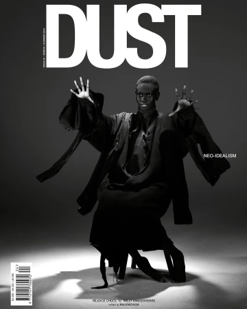 Black-and-white magazine cover featuring a dark-skinned model in an abstract pose, adorned in dark clothing, against a gray backdrop.