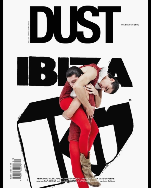 Magazine cover featuring two men in red outfits, one carrying the other, against a white background with large black typography. 