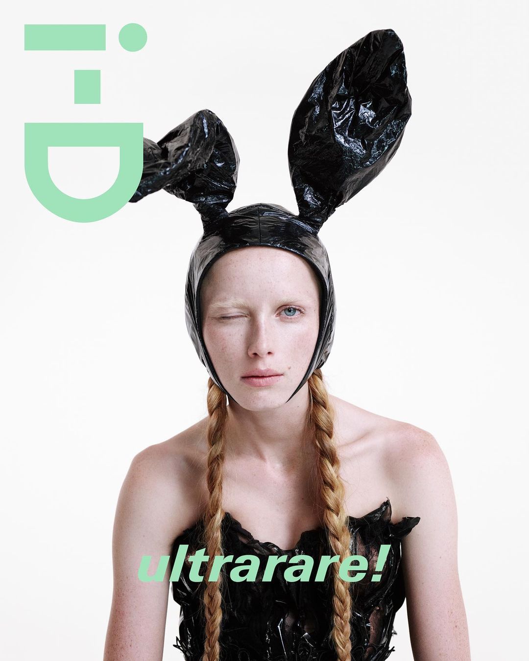 Fashion magazine cover featuring a young woman with blonde braided hair, wearing a black plastic outfit and bunny ears against white.