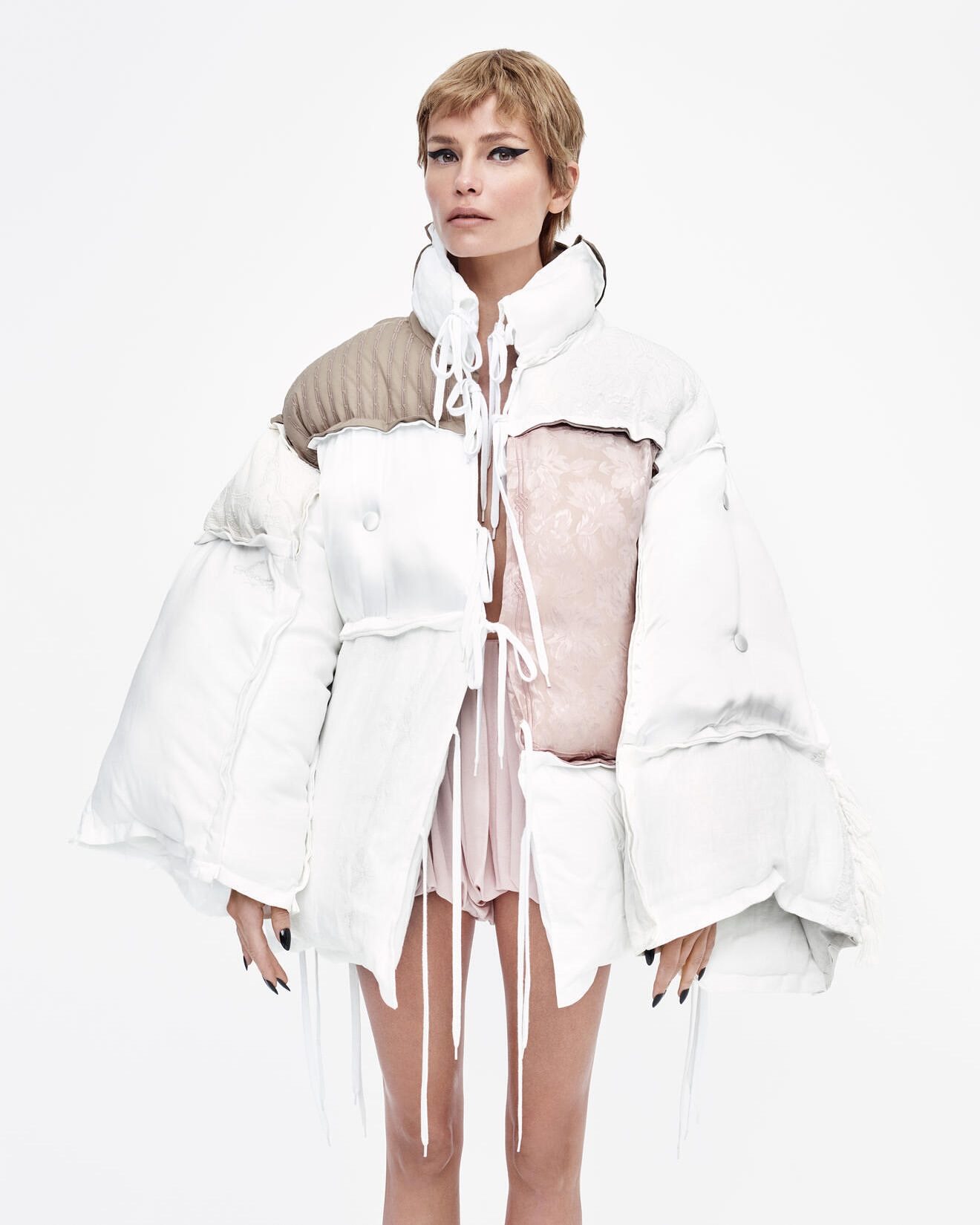 A model poses in a studio wearing an upcycled, white, deconstructed puffer jacket with neutral accents against a white background.