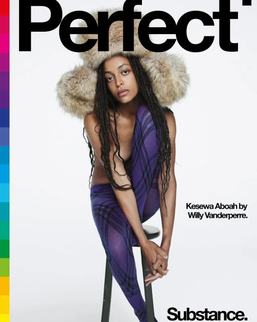 Editorial fashion shot of Kesewa Aboah in fur hat and purple plaid tights sitting on a stool against a bright white backdrop.