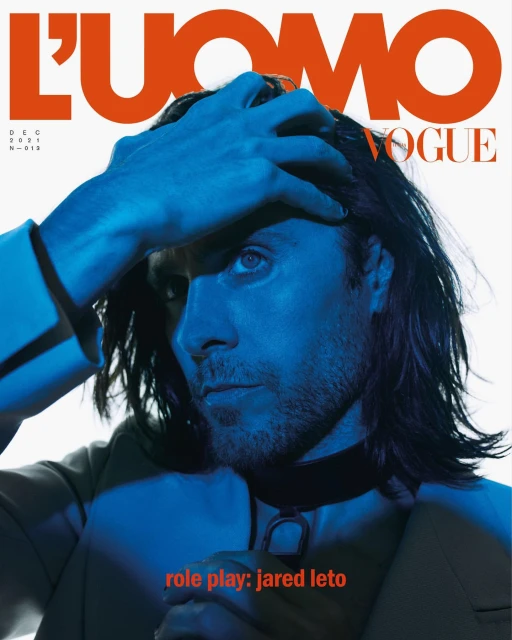 Close-up of Jared Leto on L'Uomo Vogue cover in blue lighting, wearing a collar necklace, hand on head, with orange magazine text.