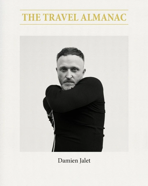 Black and white portrait of a man wearing a black top against a light background, on the cover of a book titled 'The Travel Almanac'.