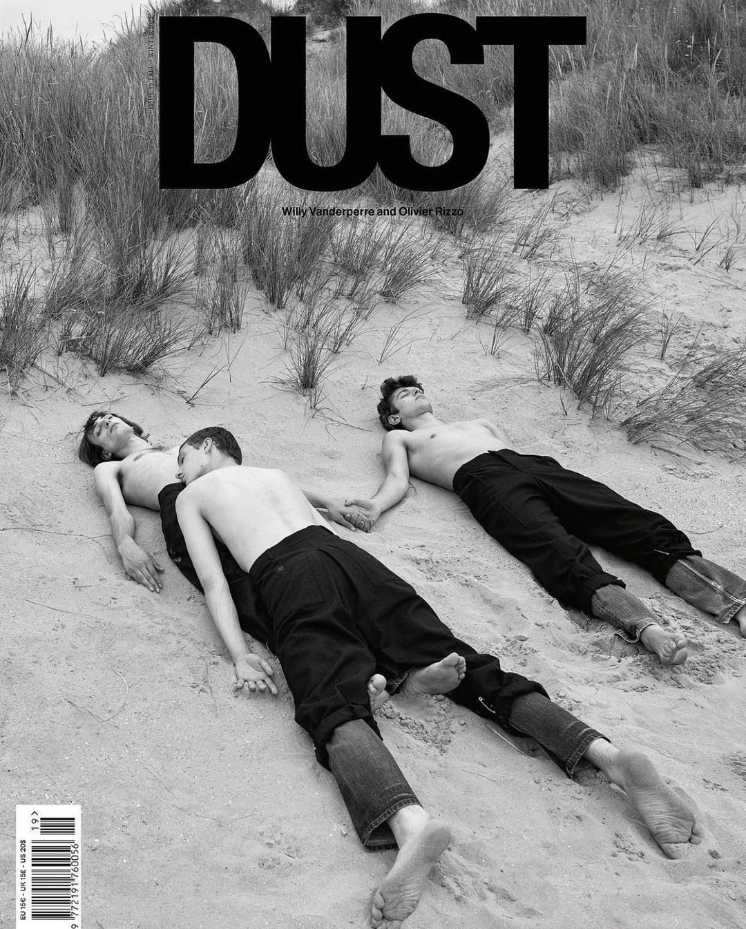 Black-and-white fashion editorial cover featuring three shirtless young men holding hands on a sandy beach with grassy dunes.
