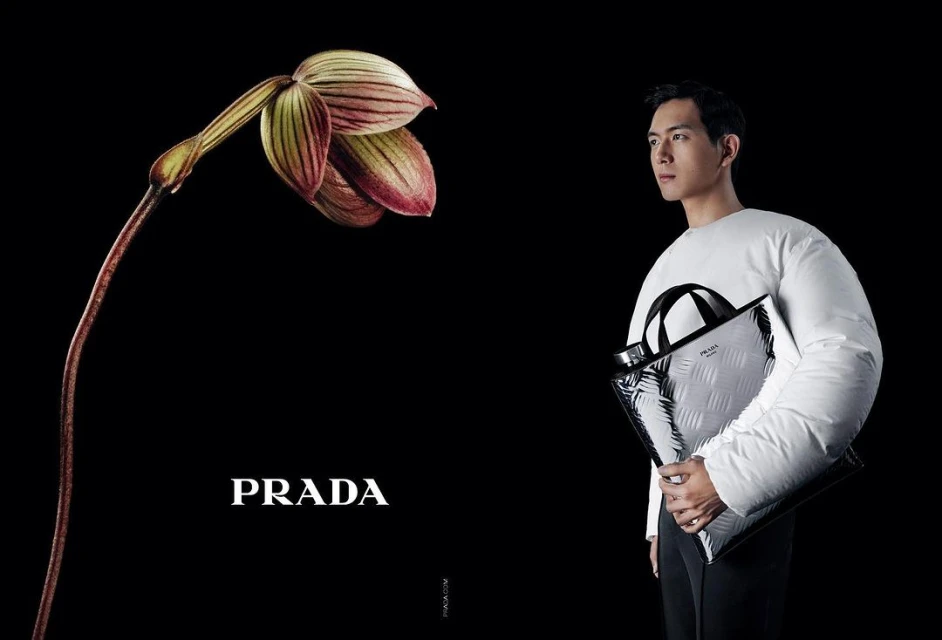 Fashion advertisement featuring a slender Asian man in a white puffy jacket, holding a Prada bag, alongside a blooming orchid on black.