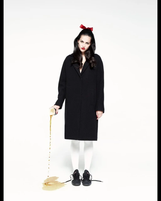 A stylish young woman with a bow poses in front of a white backdrop while intentionally spilling liquid from a can onto the floor.