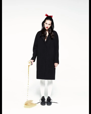 A stylish young woman with a bow poses in front of a white backdrop while intentionally spilling liquid from a can onto the floor.