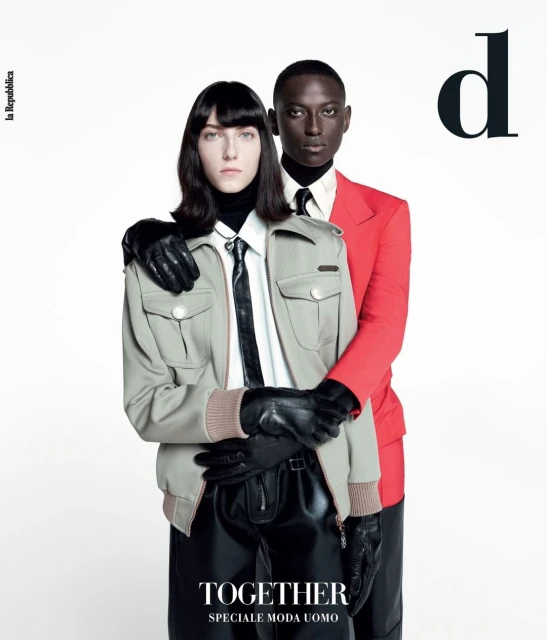 Fashion magazine cover featuring a woman in a gray jacket and a man in a red suit, both wearing black gloves against a white backdrop.