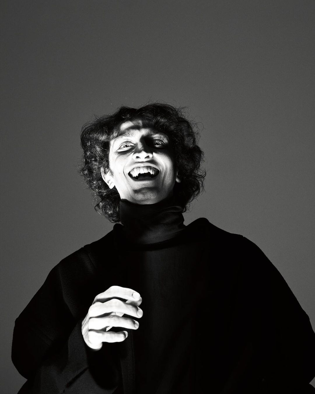 Monochrome portrait of a smiling person wearing a black turtleneck against a dark grey seamless studio background.