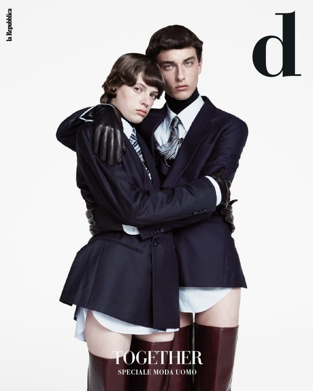 Fashion magazine cover featuring two models in dark pinstripe suits, bare legs, and high boots against a stark white background.