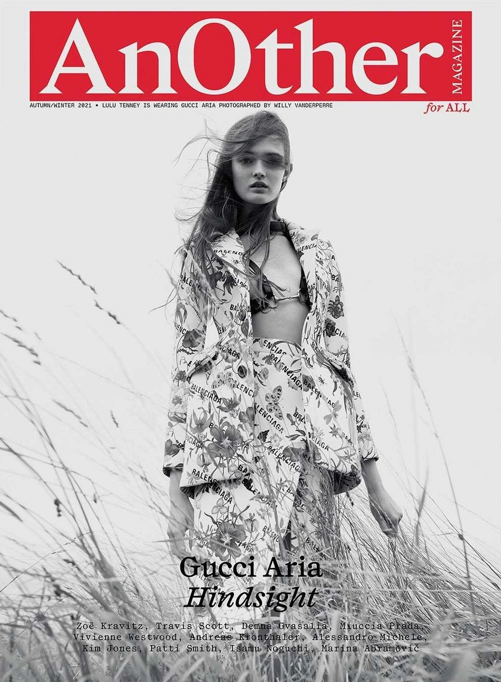 Model standing outdoors among tall grass wearing a patterned floral jacket and matching skirt photographed in black and white.
