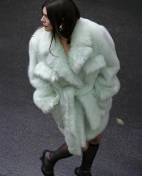 Model in mint green faux fur coat and sheer black stockings walking on wet asphalt in Paris