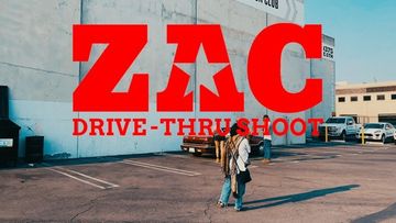 Red 'Zac Drive-Thru' graphic overlaying a sunny parking lot scene with people and cars, captured at eye-level in landscape orientation.