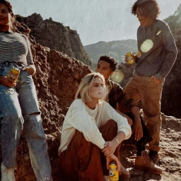 Group of four young friends relaxing outdoors amongst rocky terrain while holding canned beverages.