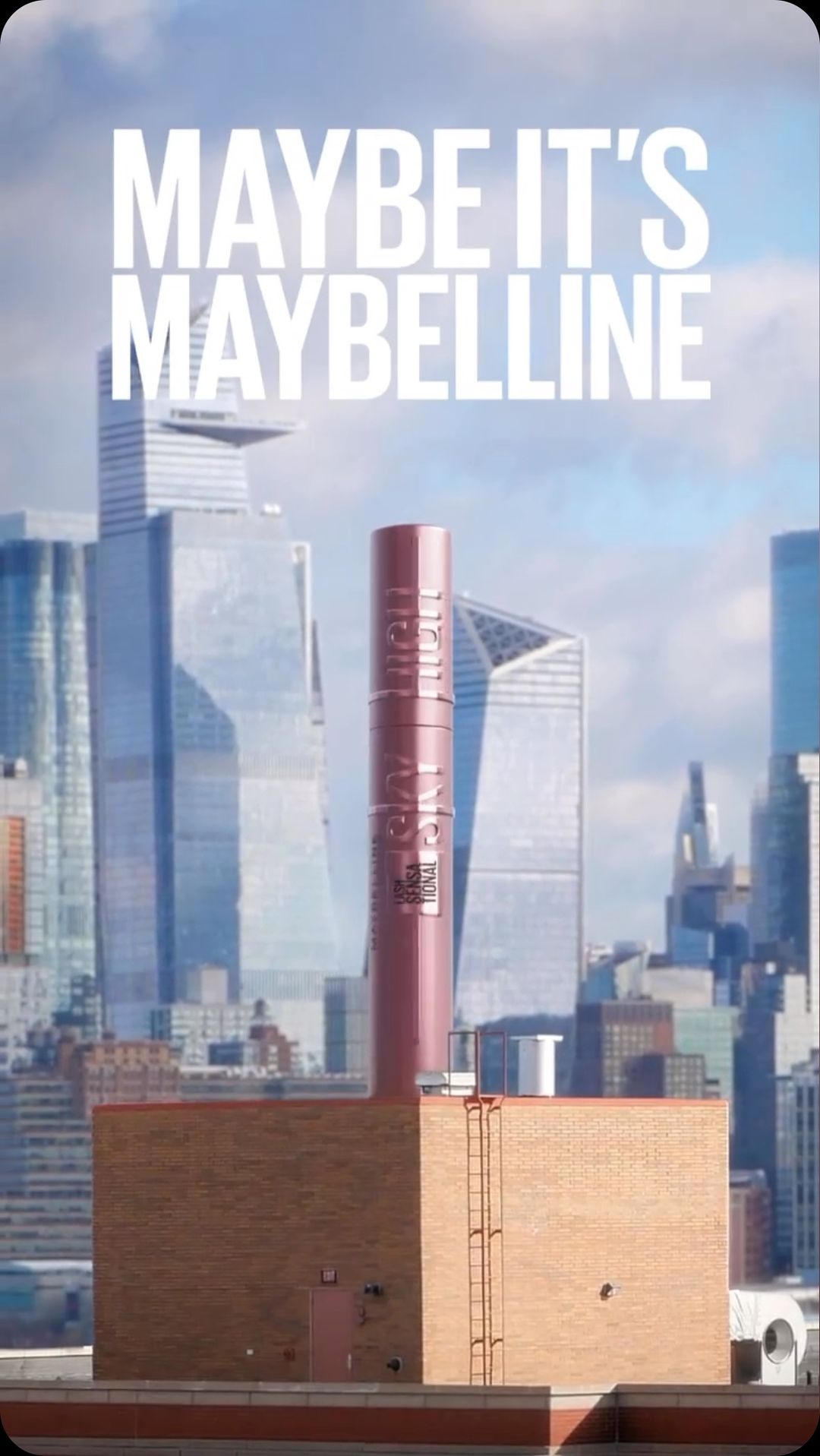 Mascara tube rises from a brick building set against a cityscape under a bright sky, with the Maybelline slogan above.