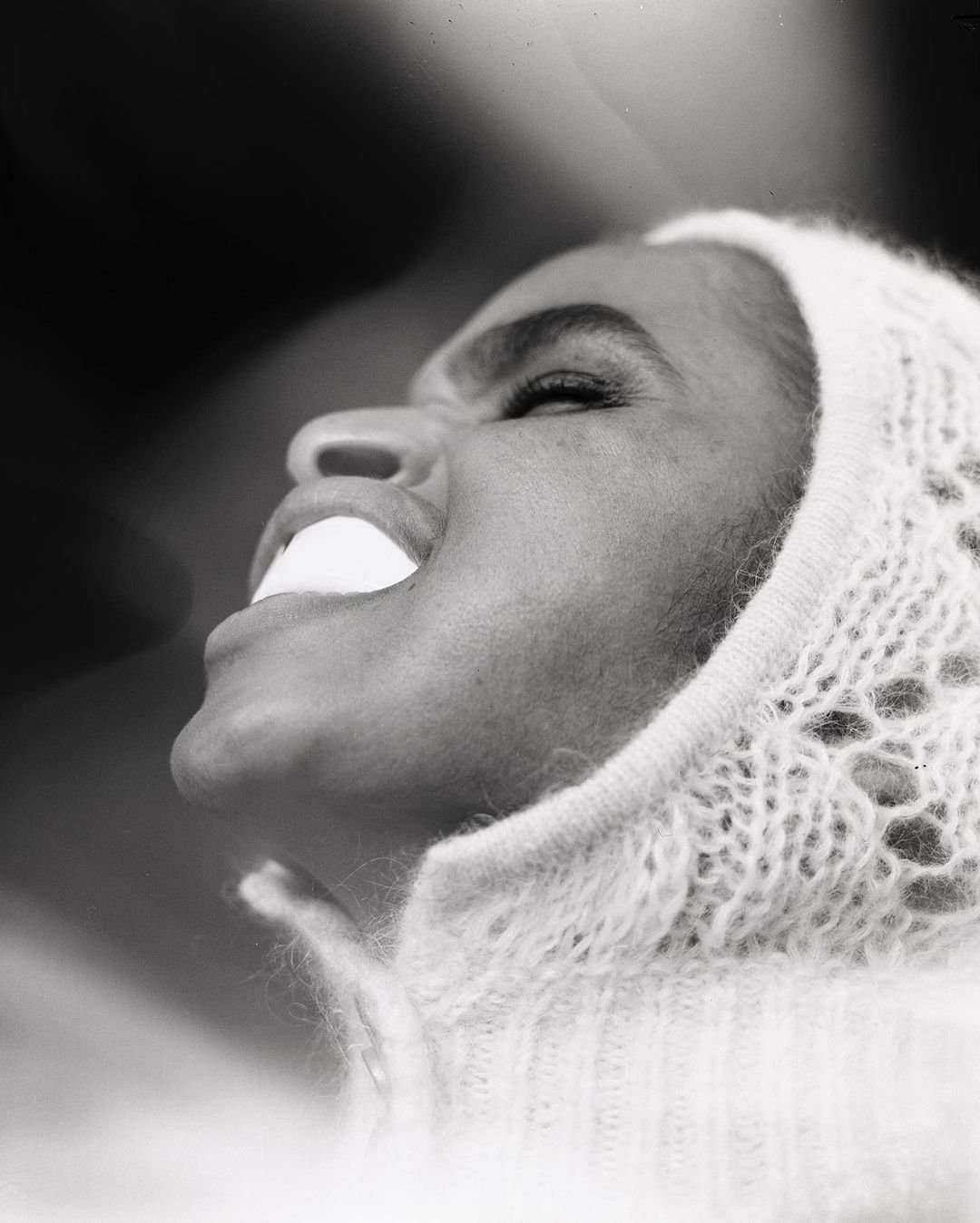 Black and white portrait of an adult female in a lace knit hood, looking up with her mouth open in a studio setting.