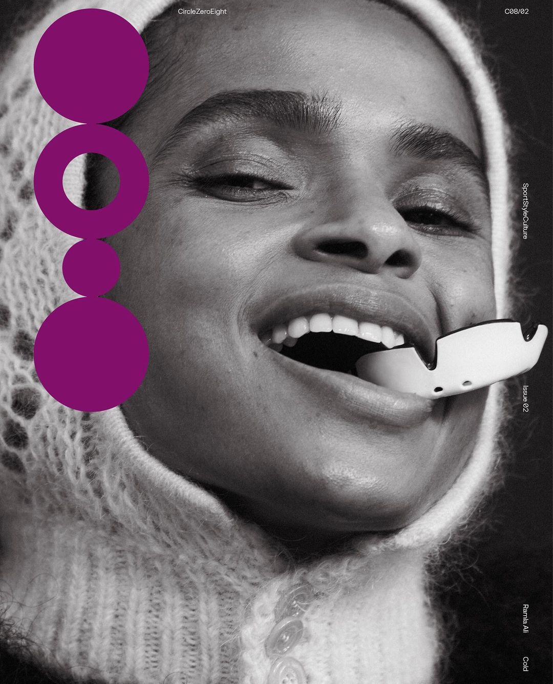 Close-up black and white portrait of a smiling woman with a white device in her mouth, wearing a fuzzy bonnet and magenta circle shapes.