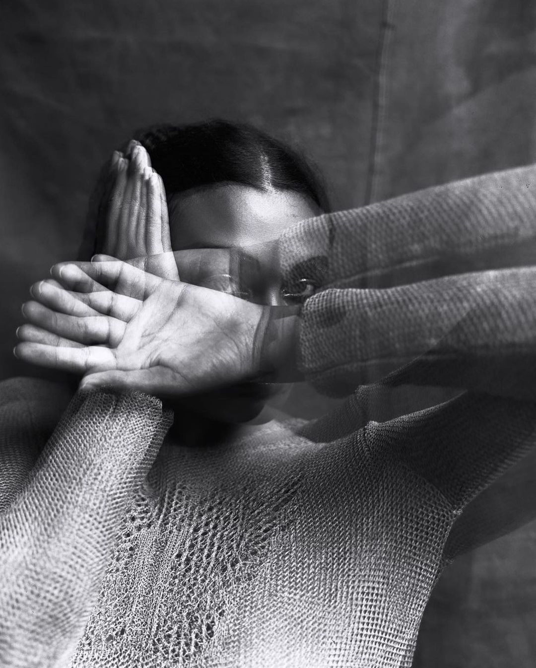 Black and white artistic portrait of an adult female shielding her face with her hands in a blurry, long-exposure indoor setting.