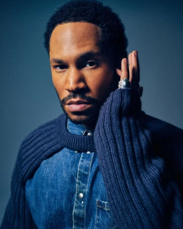 Portrait of a black man with short dark hair and facial hair wearing a blue denim shirt and a ribbed navy sweater, photographed by Xavier Scott Marshall.