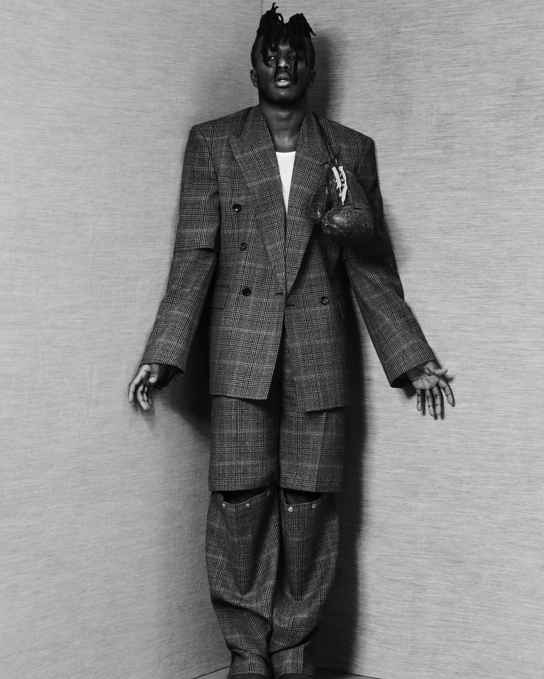 Black and white studio shot of a slender, black male model wearing a double-breasted suit with boxing gloves over his shoulder.