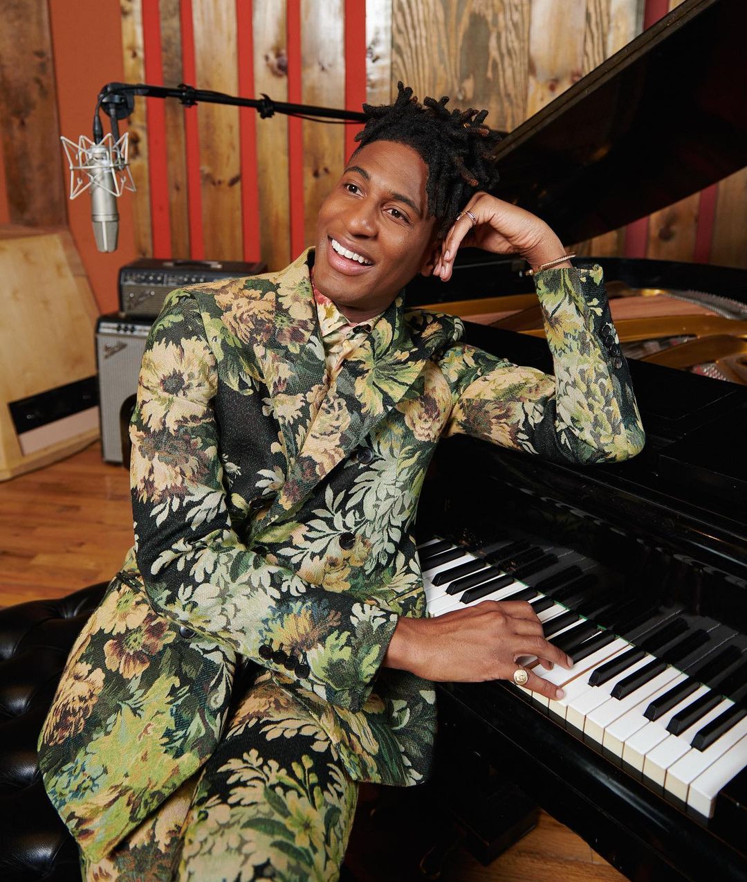 Smiling man in floral suit sits at grand piano in recording studio with microphone. Music performance, portrait, lifestyle shoot.