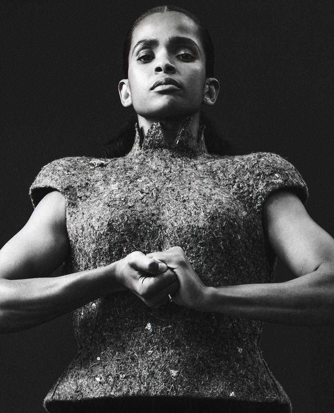 Low angle monochrome portrait of a woman wearing a textured high neck structured top with clasped hands